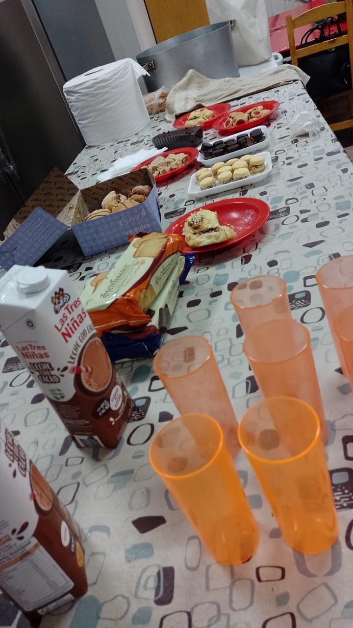 Mesa de buffet con platos de comida, vasos y servilletas en una reunión informal en interiores.