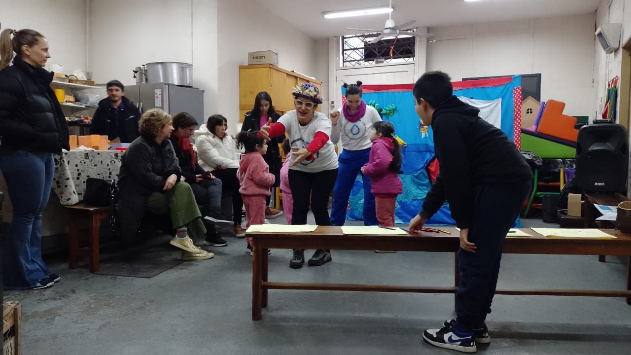 Varias personas reunidas en una habitación juegan alrededor de una mesa baja, con coloridas decoraciones de fondo.
