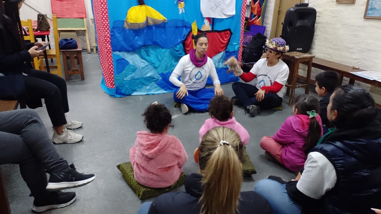 El grupo de la hora del cuento se sienta en el suelo frente a un orador sentado en un aula colorida.