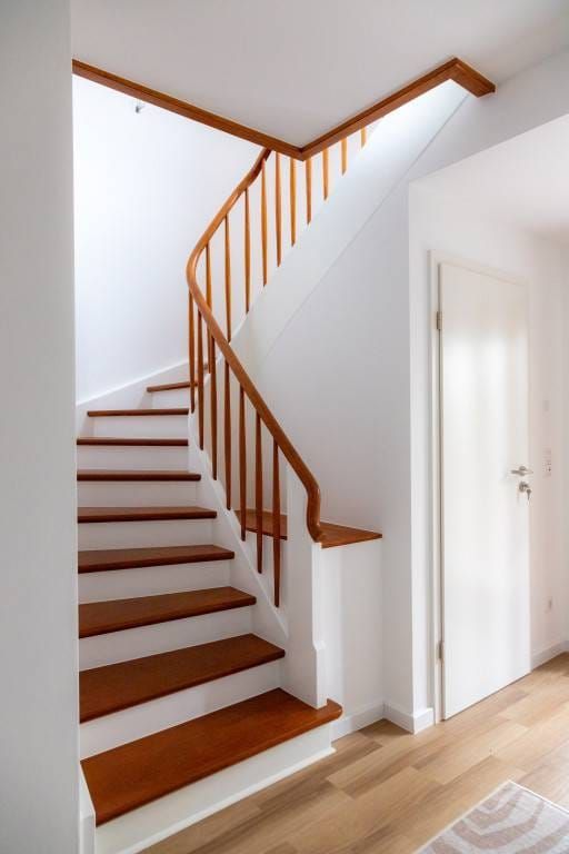Eine Holz-Treppe nach oben mit weißen Stufen und einem braunen Geländer