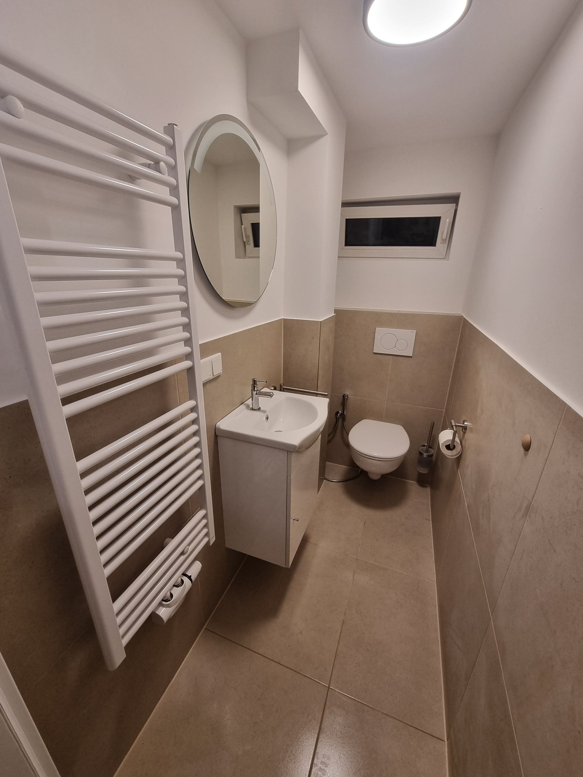 Ein fertig renoviertes Bad mit weißen Wanden, Heizung und Spiegel.