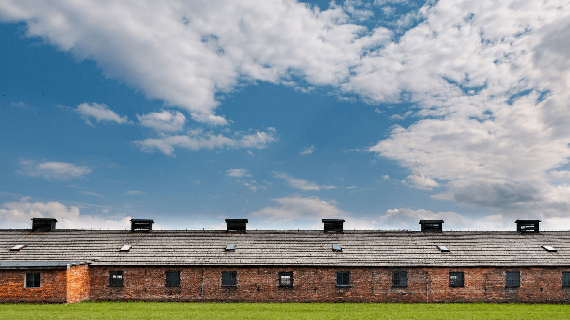 Brick barracks at Auschwitz-Birkenau under a clear sky.