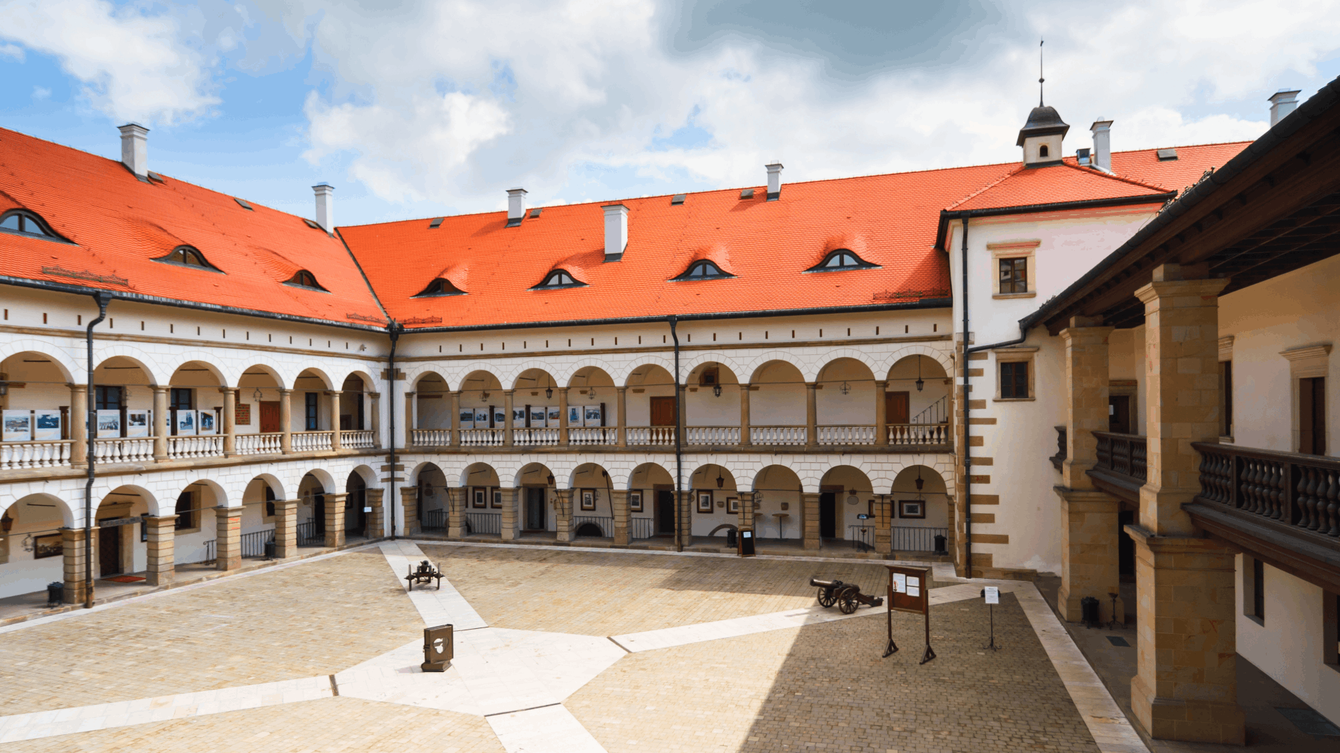 Historic Krakow building with manicured flower beds in front, shown in bright summer light.