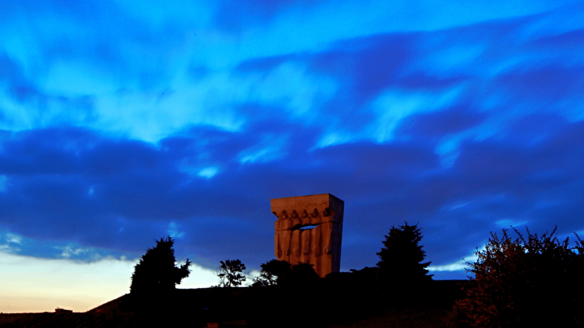 Stone monument at Plaszów camp under a dramatic blue sky