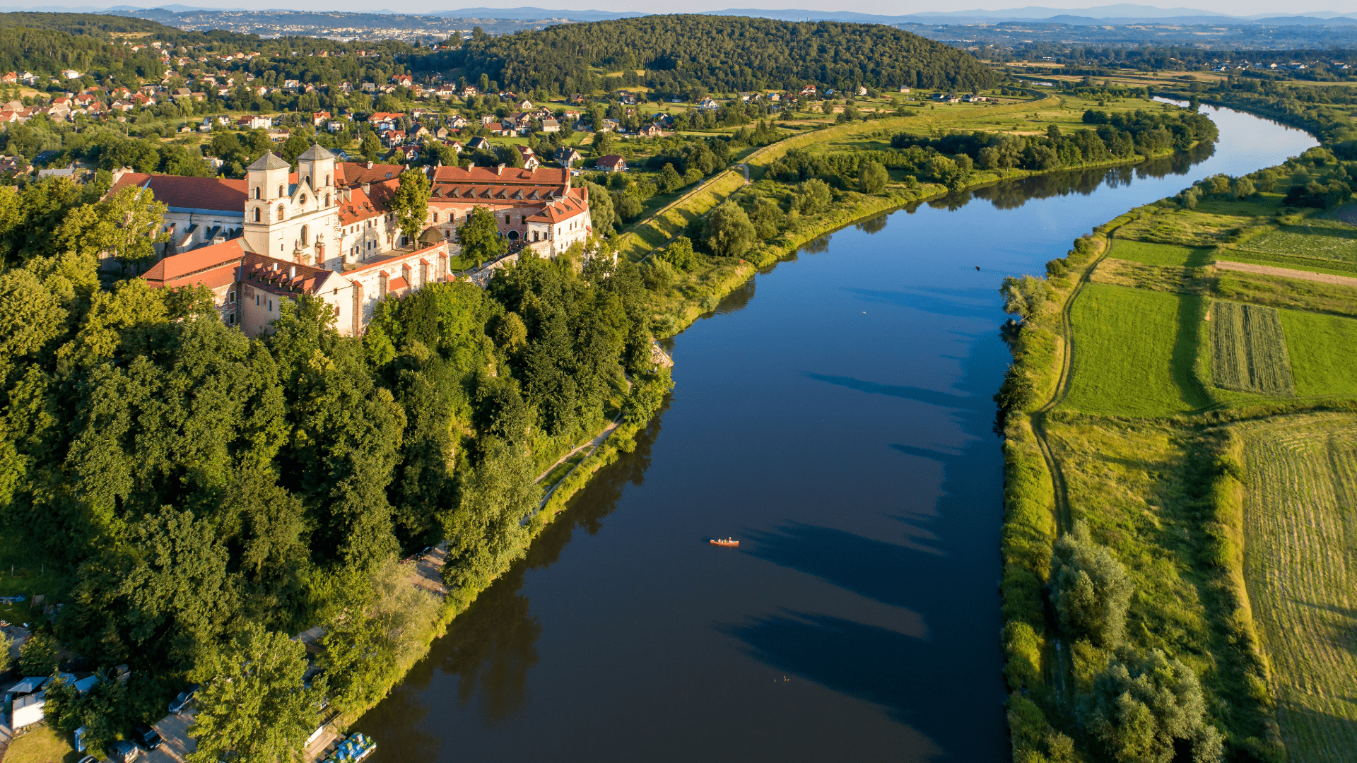 Aerial view of a river surrounded by lush greenery and a monastery on the bank near Kraków