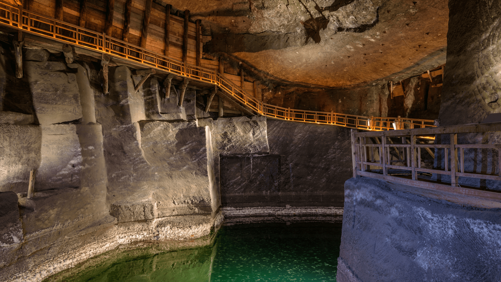 Underground chamber in Wieliczka Salt Mine with water and a lit walkway.
