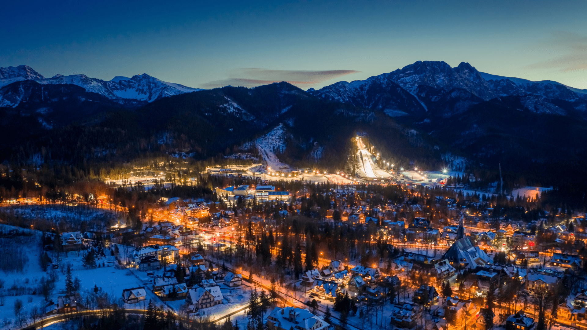 Night view of Zakopane town lit up across a mountain valley