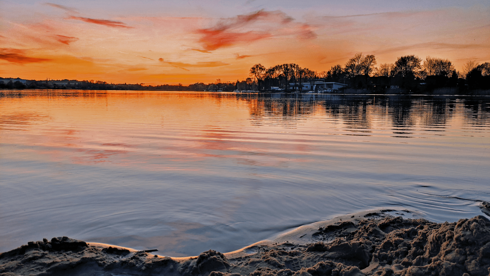 Picturesque sunset over a calm river with boats and distant trees on the horizon