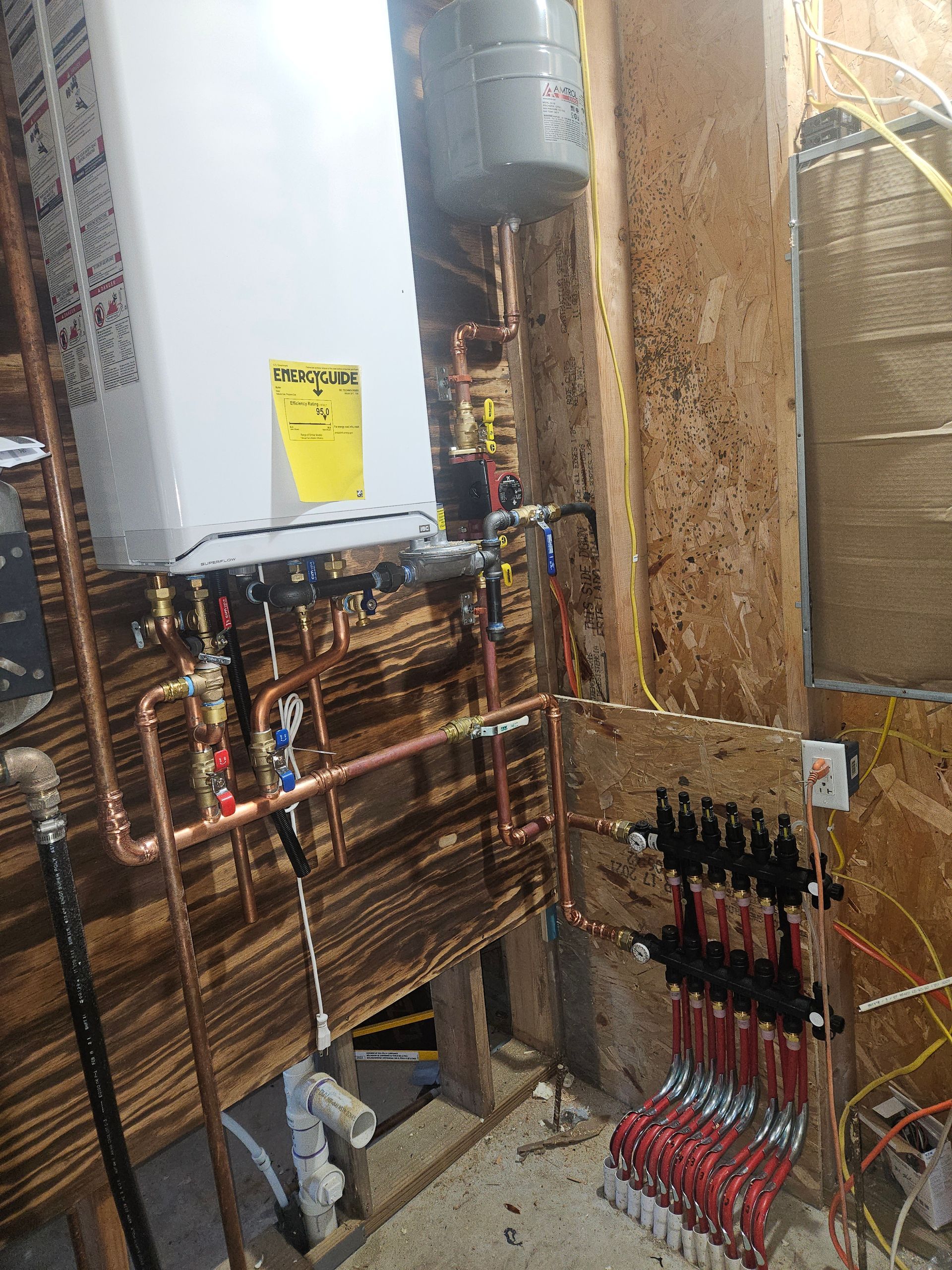 A boiler is sitting on top of a wooden wall next to copper pipes.