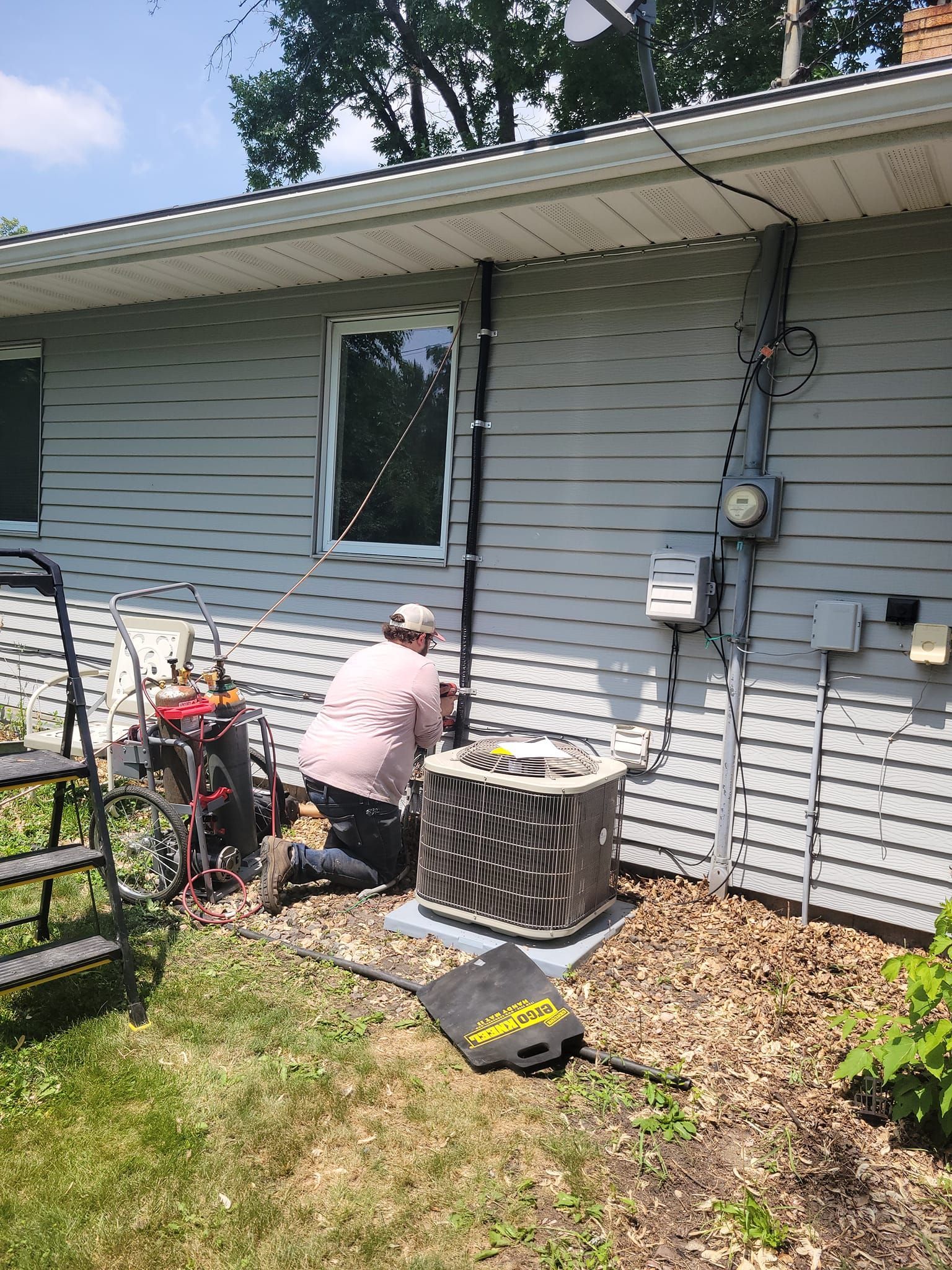 A man is working on an air conditioner outside of a house.