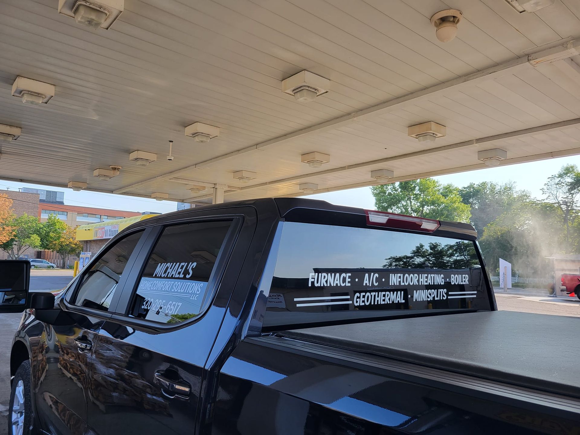 A black truck is parked under a canopy at a gas station.
