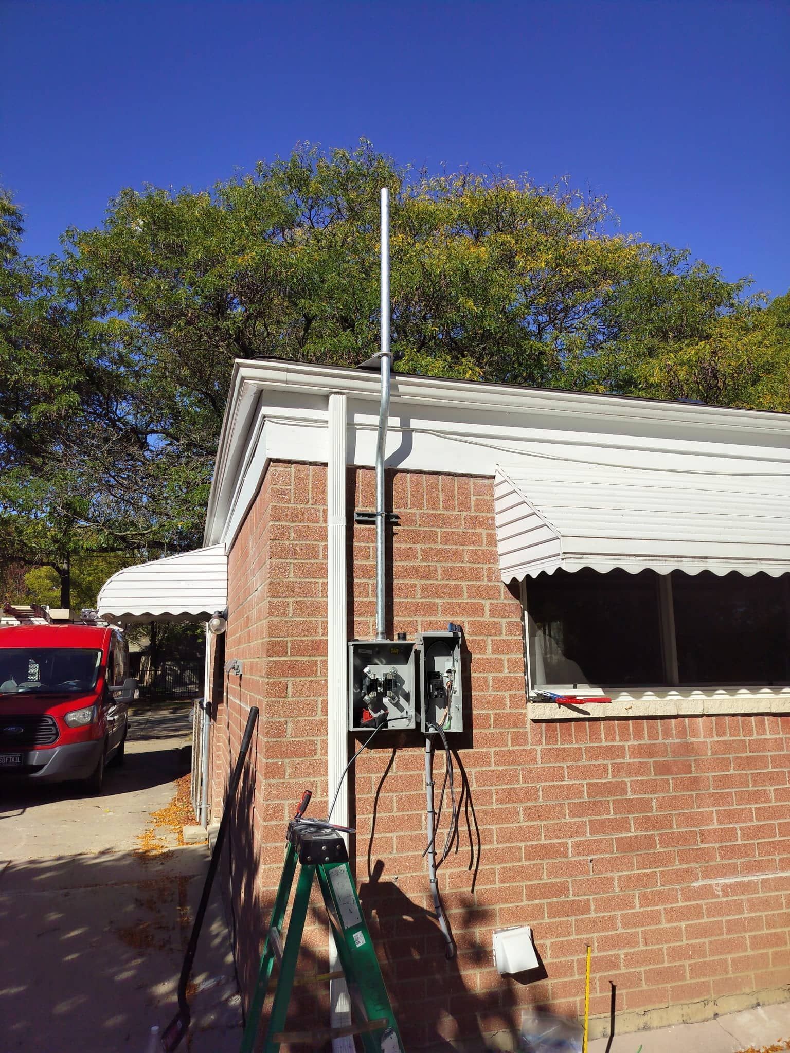 Brick utility building with tall white pole, green ladder, and electrical boxes under a blue sky