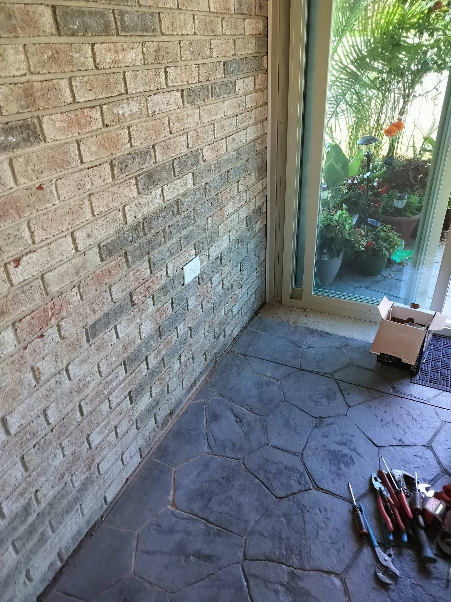 Brick wall and slate floor in a patio corner, with garden plants visible through an open doorway.