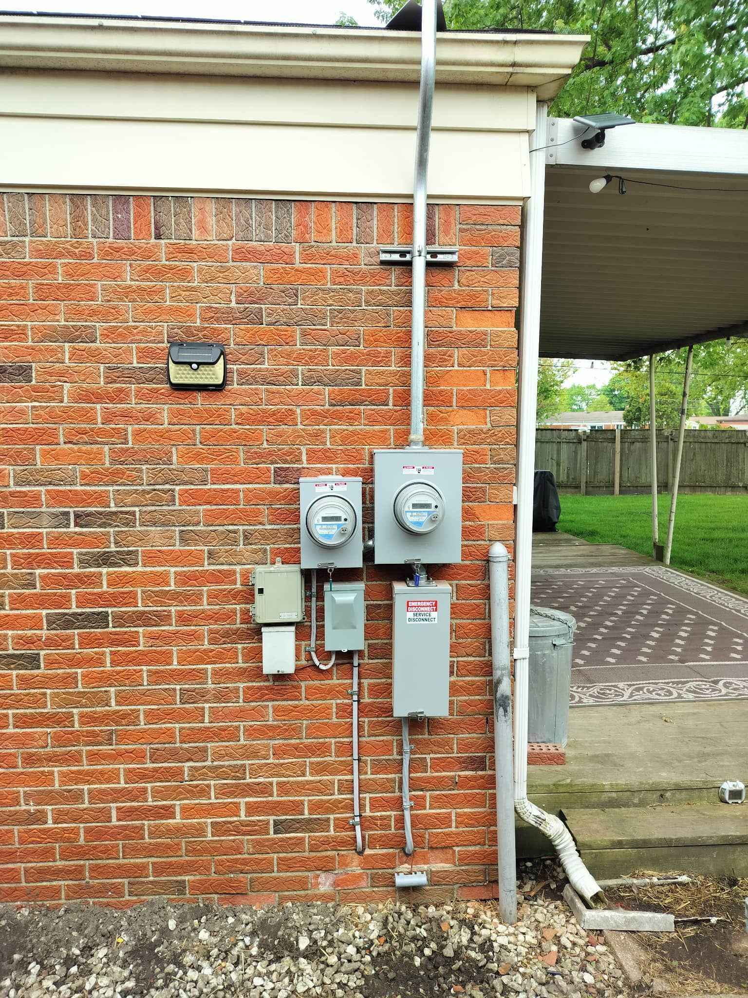 Brick exterior wall with utility meters and conduit beside a driveway and fence