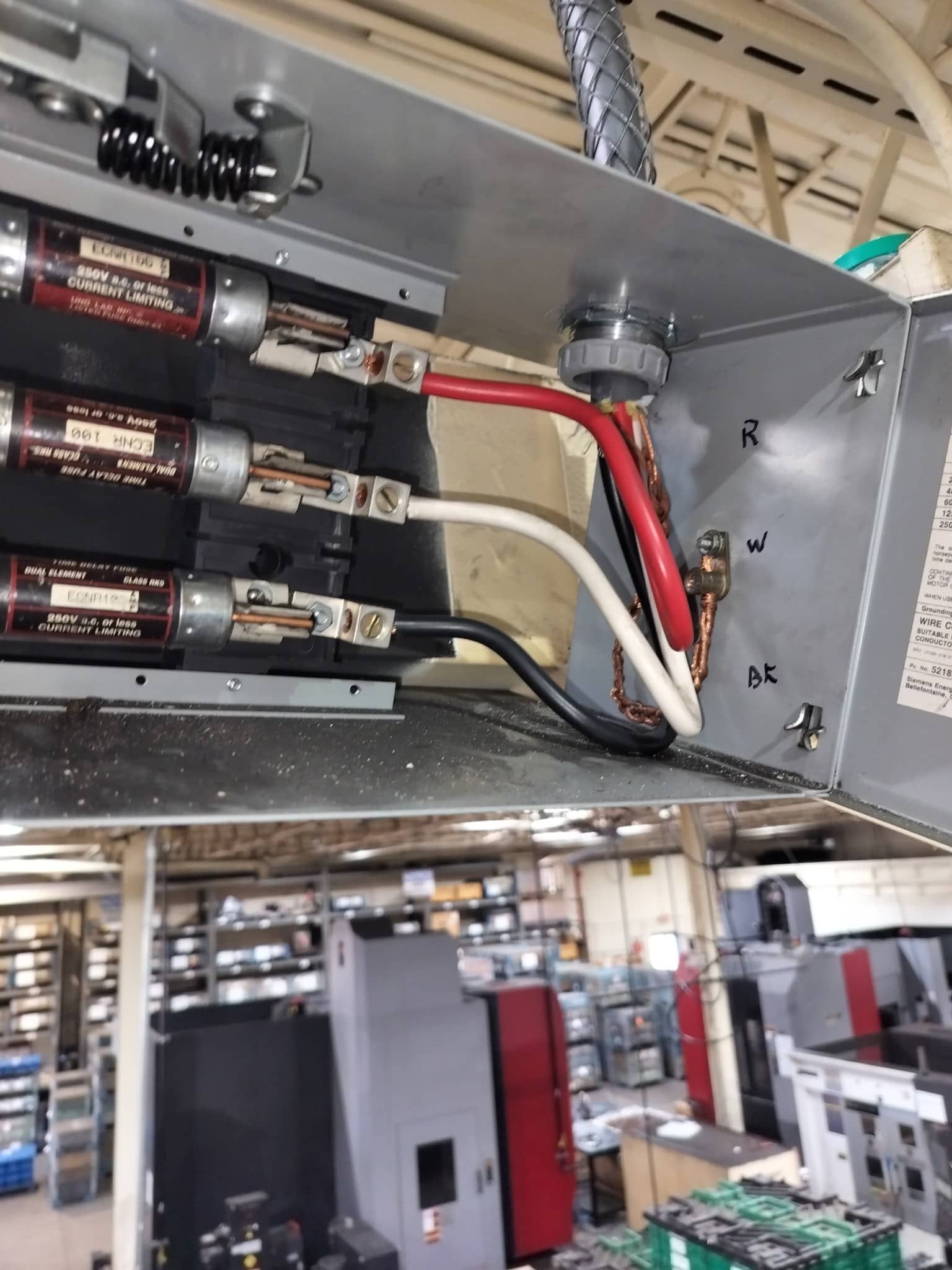 Electrical control panel interior with fuses, red and white wires, and industrial equipment below