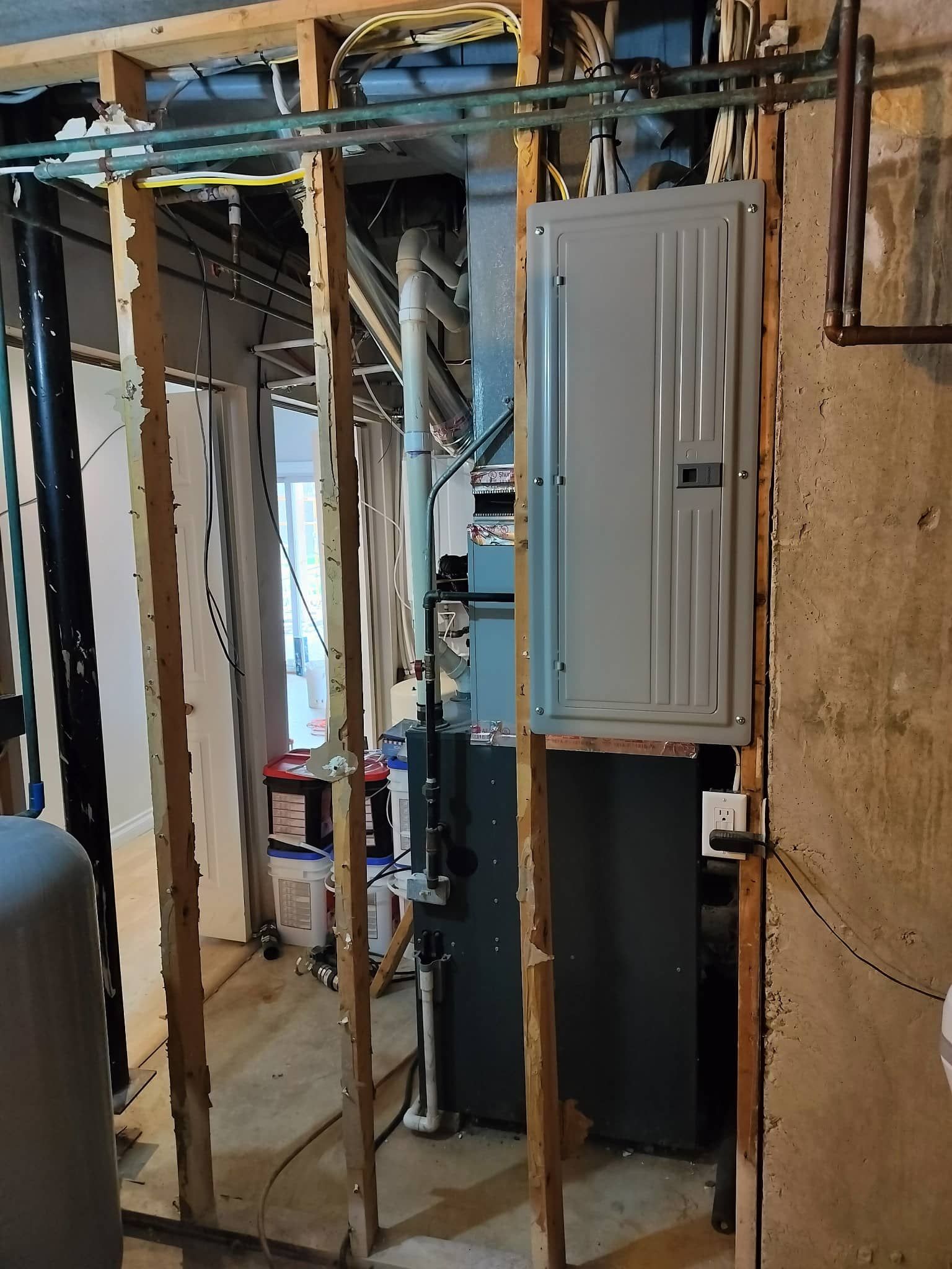 Unfinished basement utility area with exposed framing, pipes, and an electrical panel.