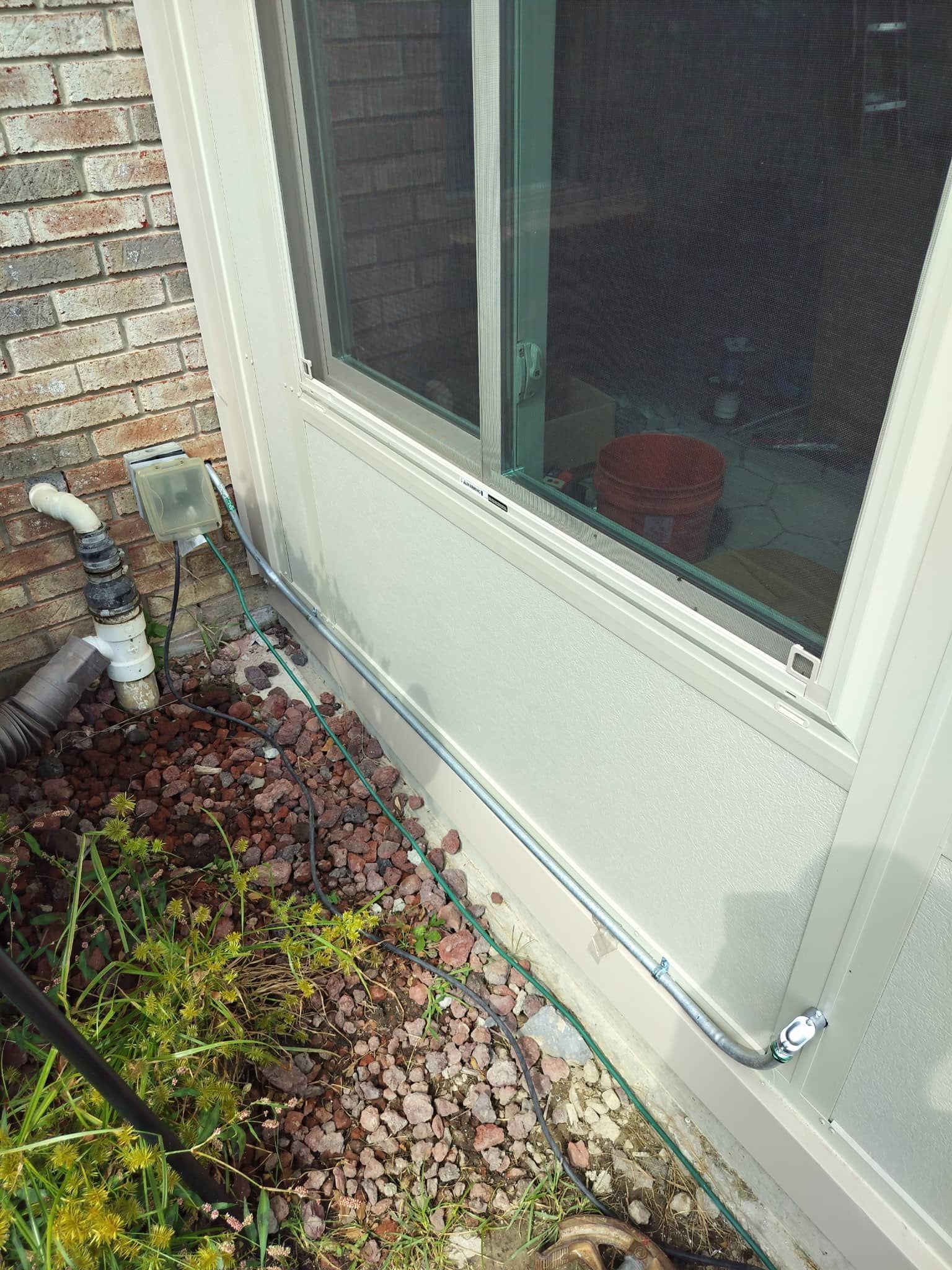 Exterior wall with a window, exposed pipes, and wet leaves along the foundation.