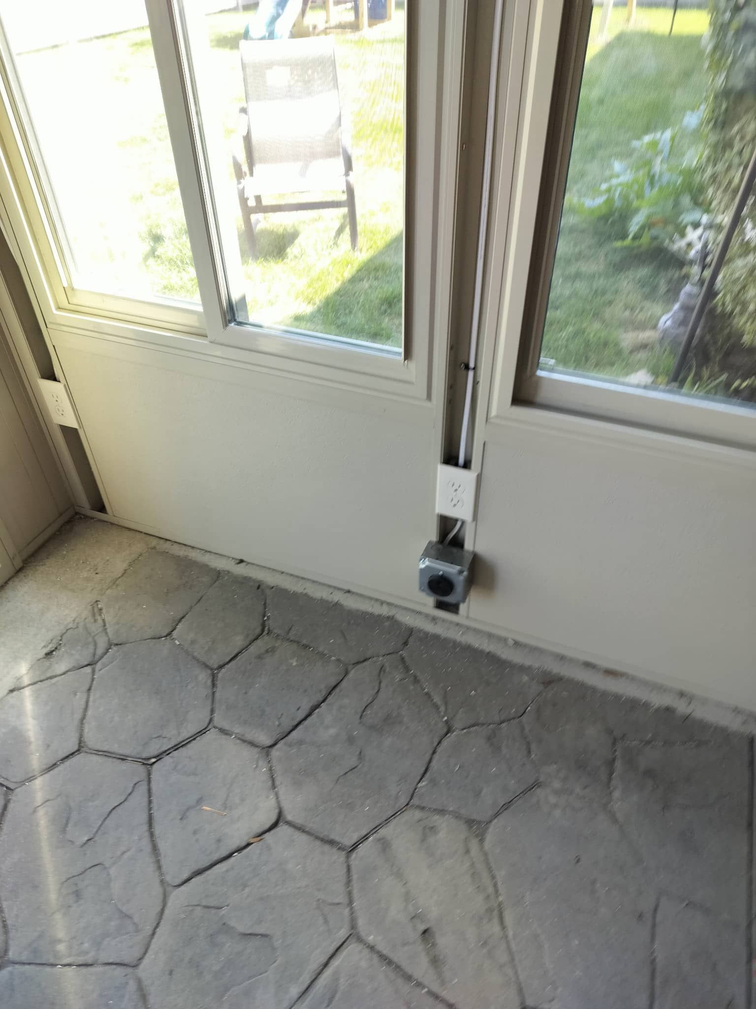 Closed glass door with a small black device mounted at the bottom, beside a windowed patio area.