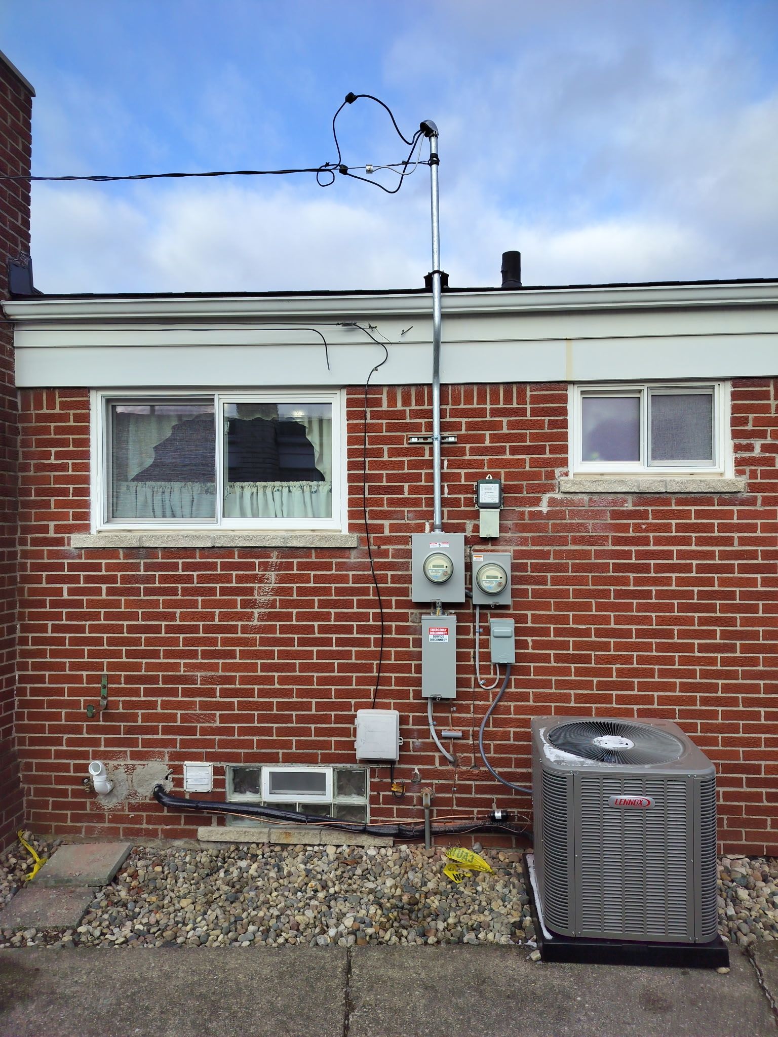 Brick house exterior with utility meters, pipes, and an HVAC unit beside a gravel yard
