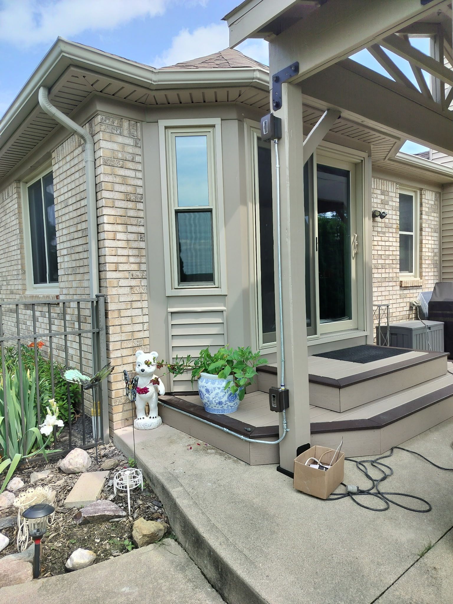 Brick house patio with steps, potted flowers, and a small garden beside a concrete walkway