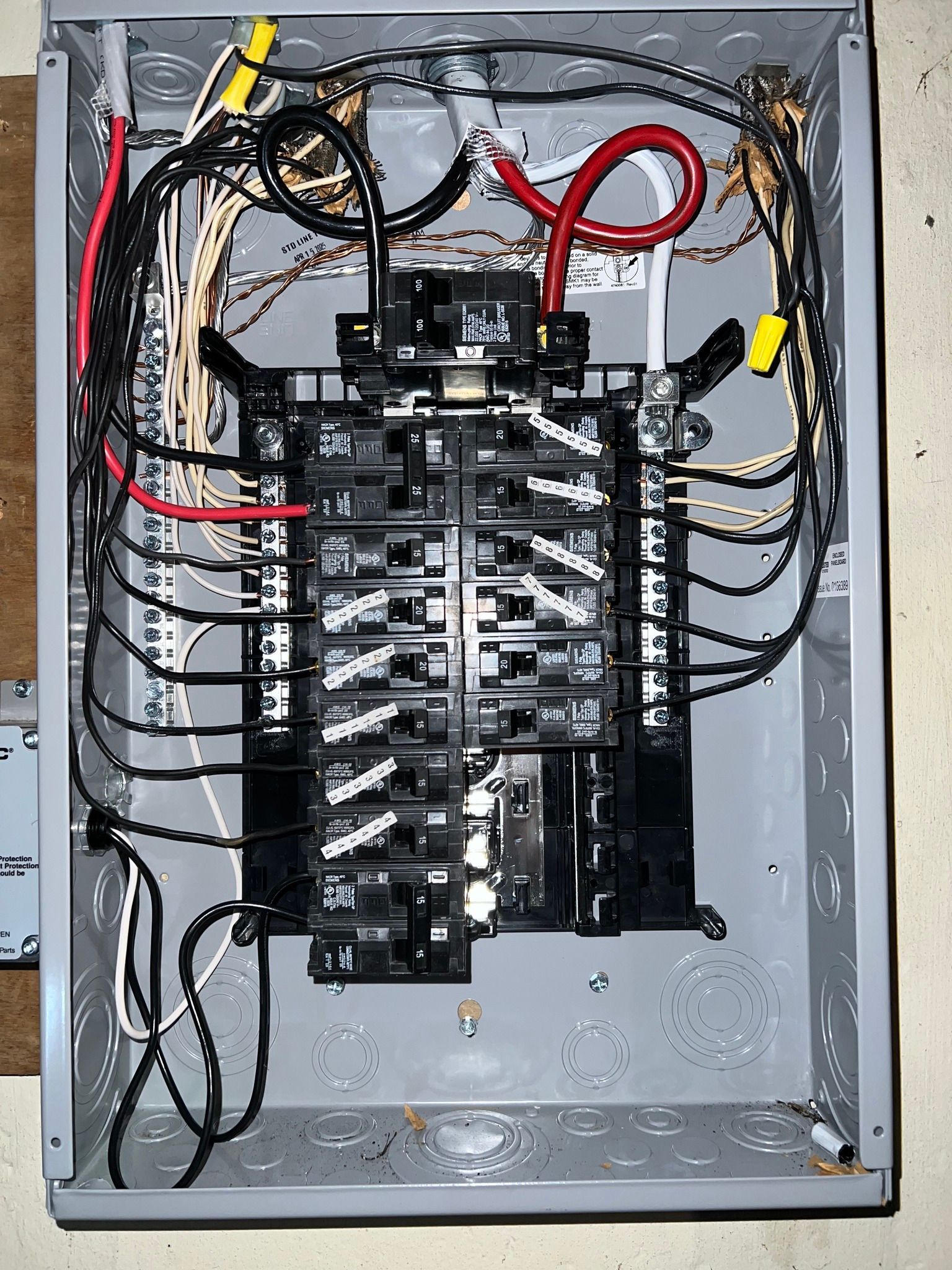 Open electrical breaker panel with many black wires and red cables inside a gray metal box