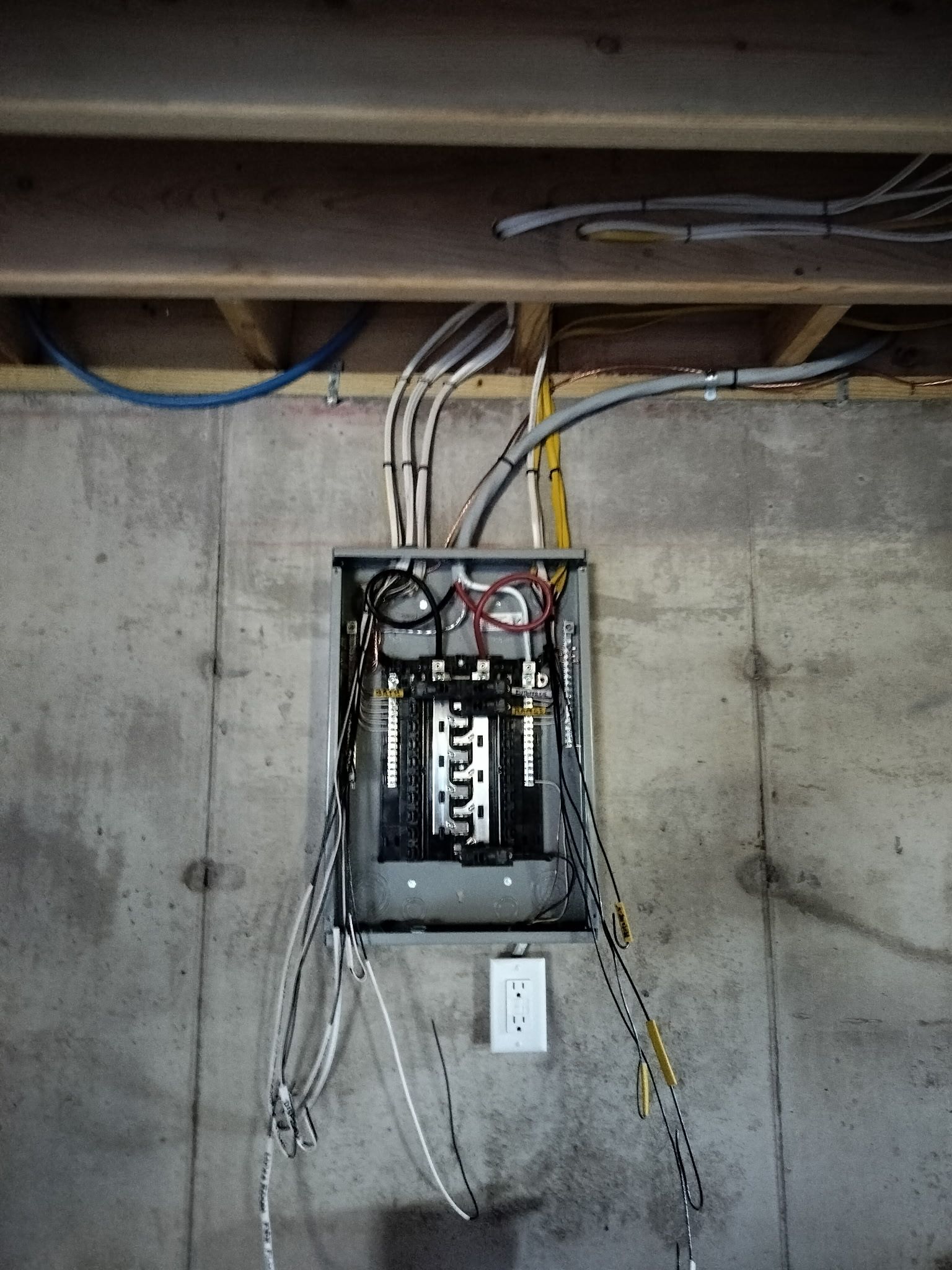 Open electrical breaker panel in a concrete wall with exposed wires and conduit.