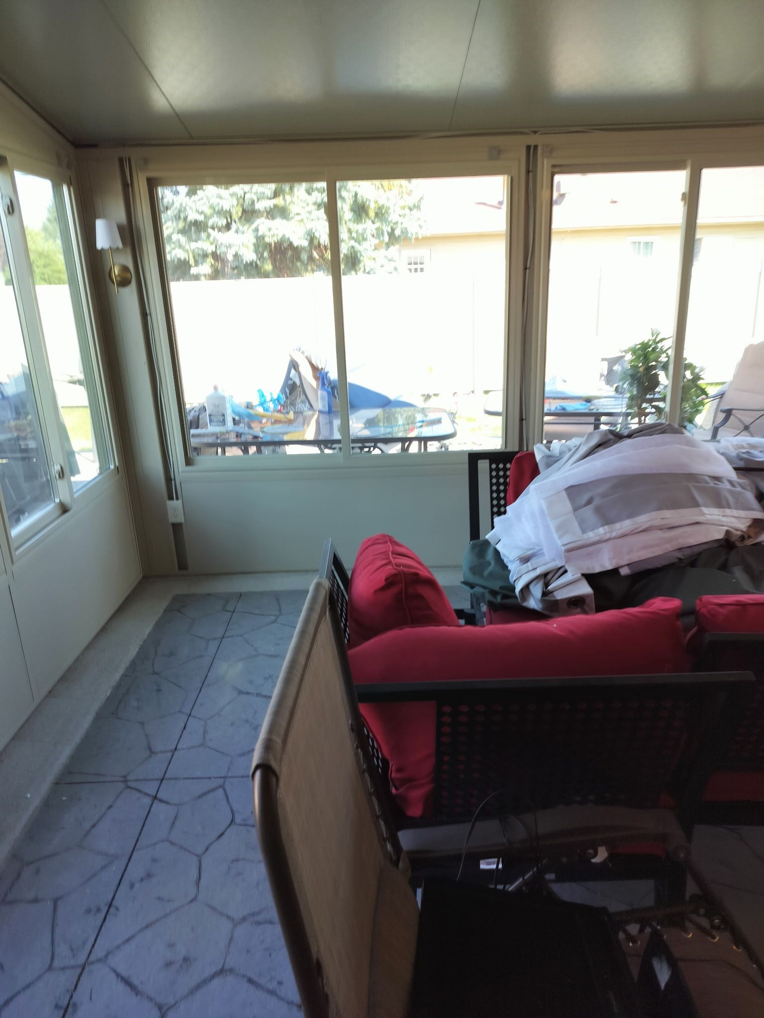 Sunroom with red-cushioned wicker sofa, tiled floor, and bright windows overlooking a patio