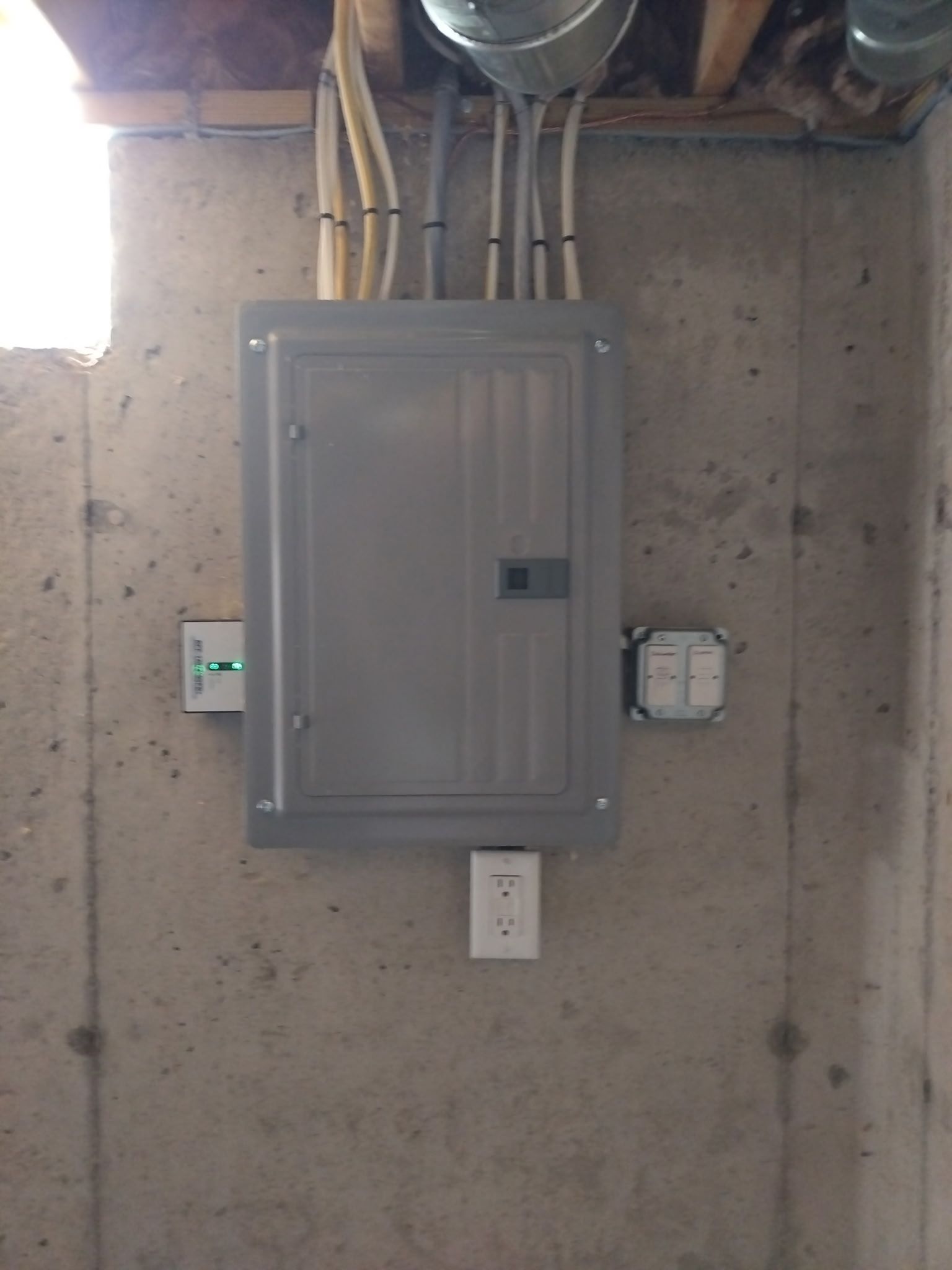 Gray electrical panel mounted on a concrete wall with conduit pipes above and outlets below