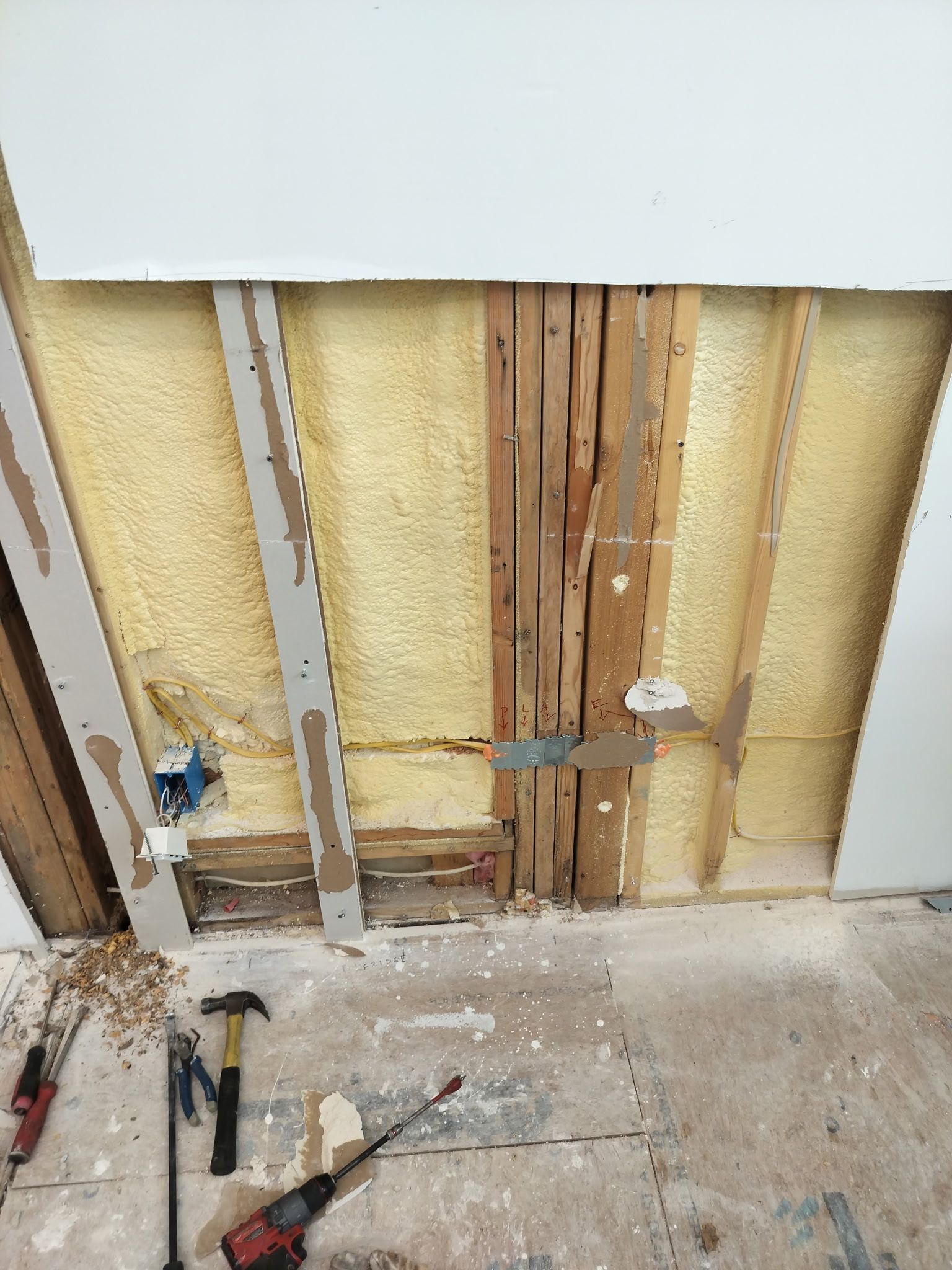Partially stripped wall with exposed studs and insulation during renovation, tools on the floor