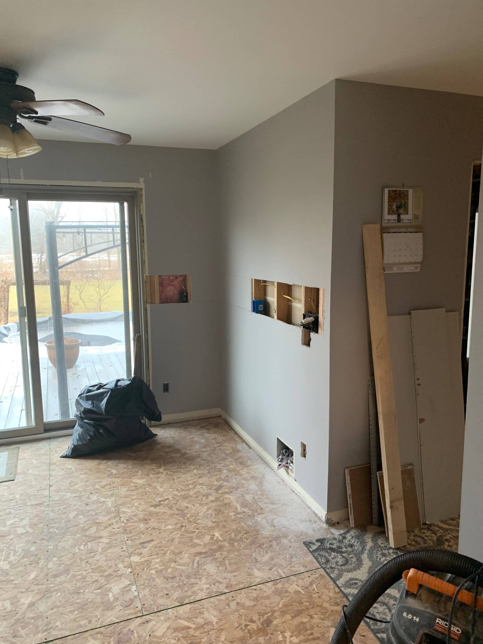 Unfinished room with exposed subfloor, sliding glass door, wall cutouts, and renovation materials.