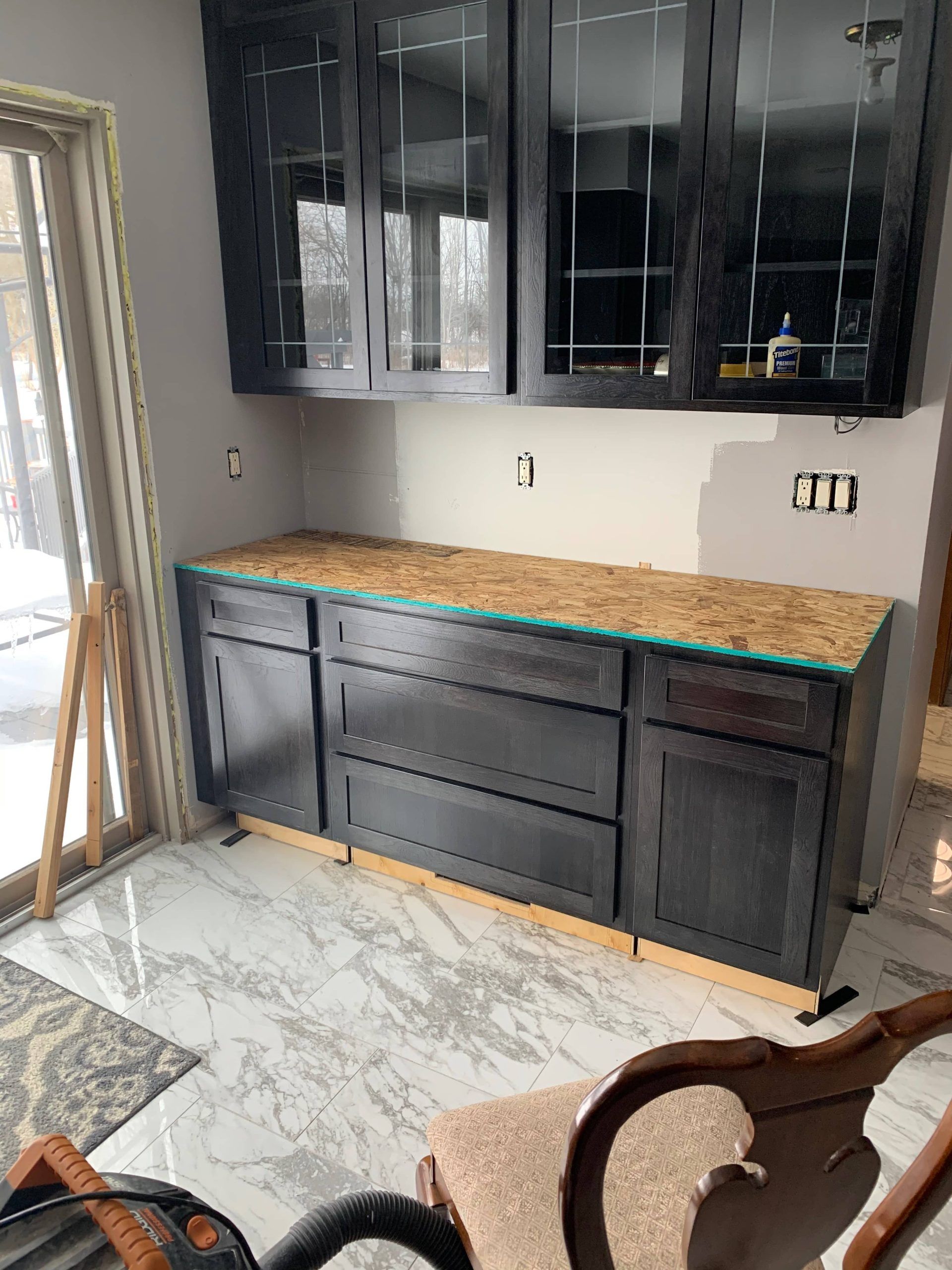 Modern kitchen with dark cabinets, wood countertop, and white marble floor near a sliding glass door