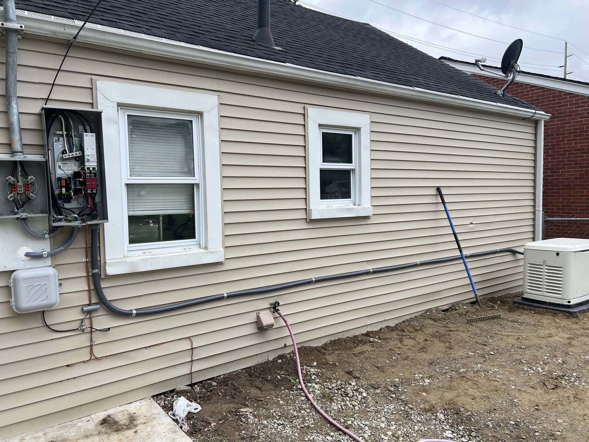 House exterior with beige vinyl siding, two windows, utility meters, and an air conditioner unit along the wall