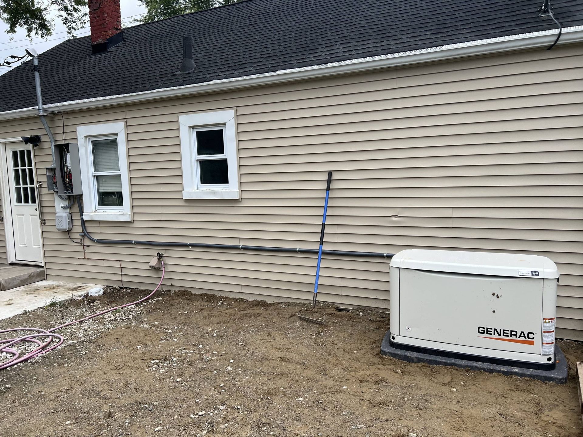 House exterior with tan siding, windows, a door, and a white Generac generator on the right