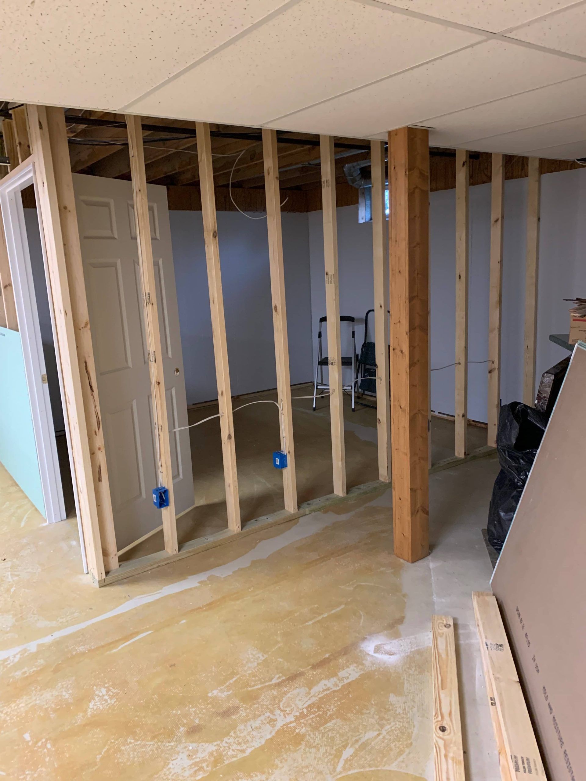 Partially demolished room with exposed wall studs, unfinished floor, and ceiling tiles.