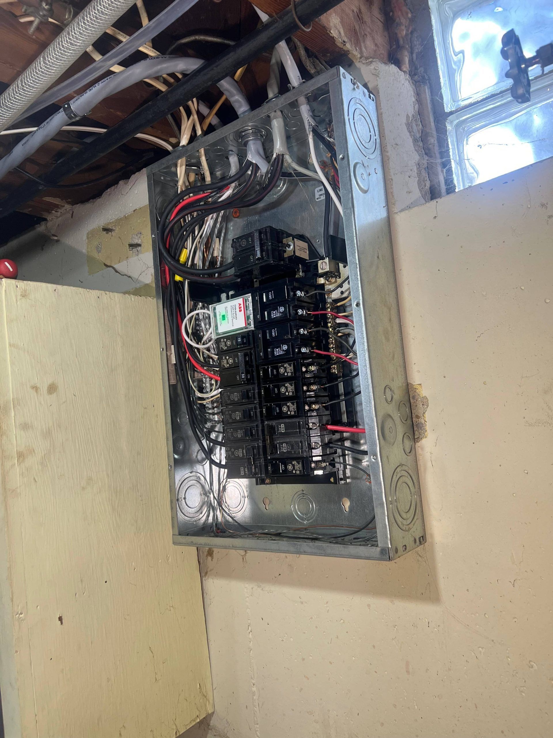 Electrical breaker panel mounted on a wall in a basement with exposed rafters above