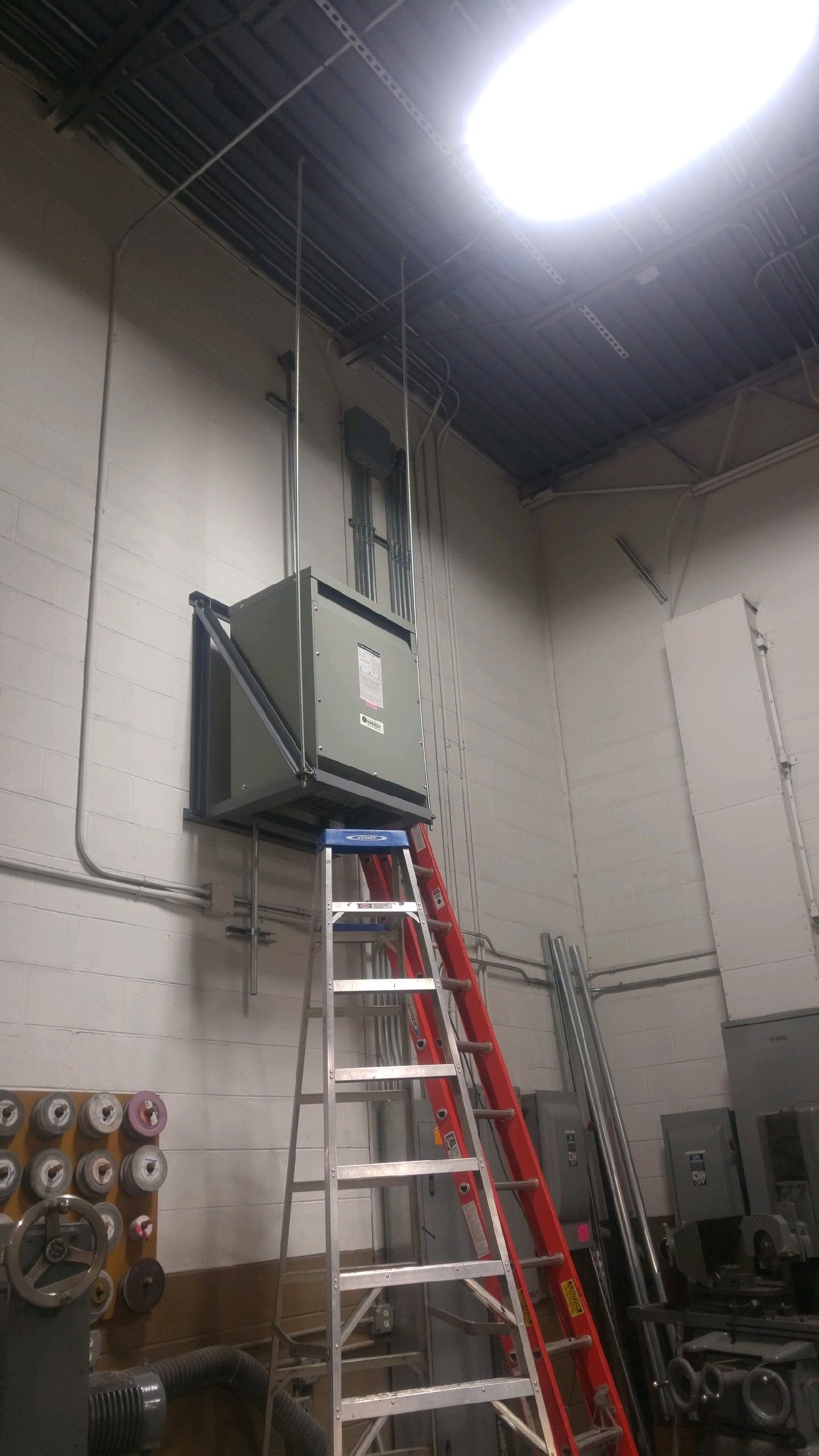Industrial room with a ladder under a ceiling-mounted electrical unit and bright overhead light