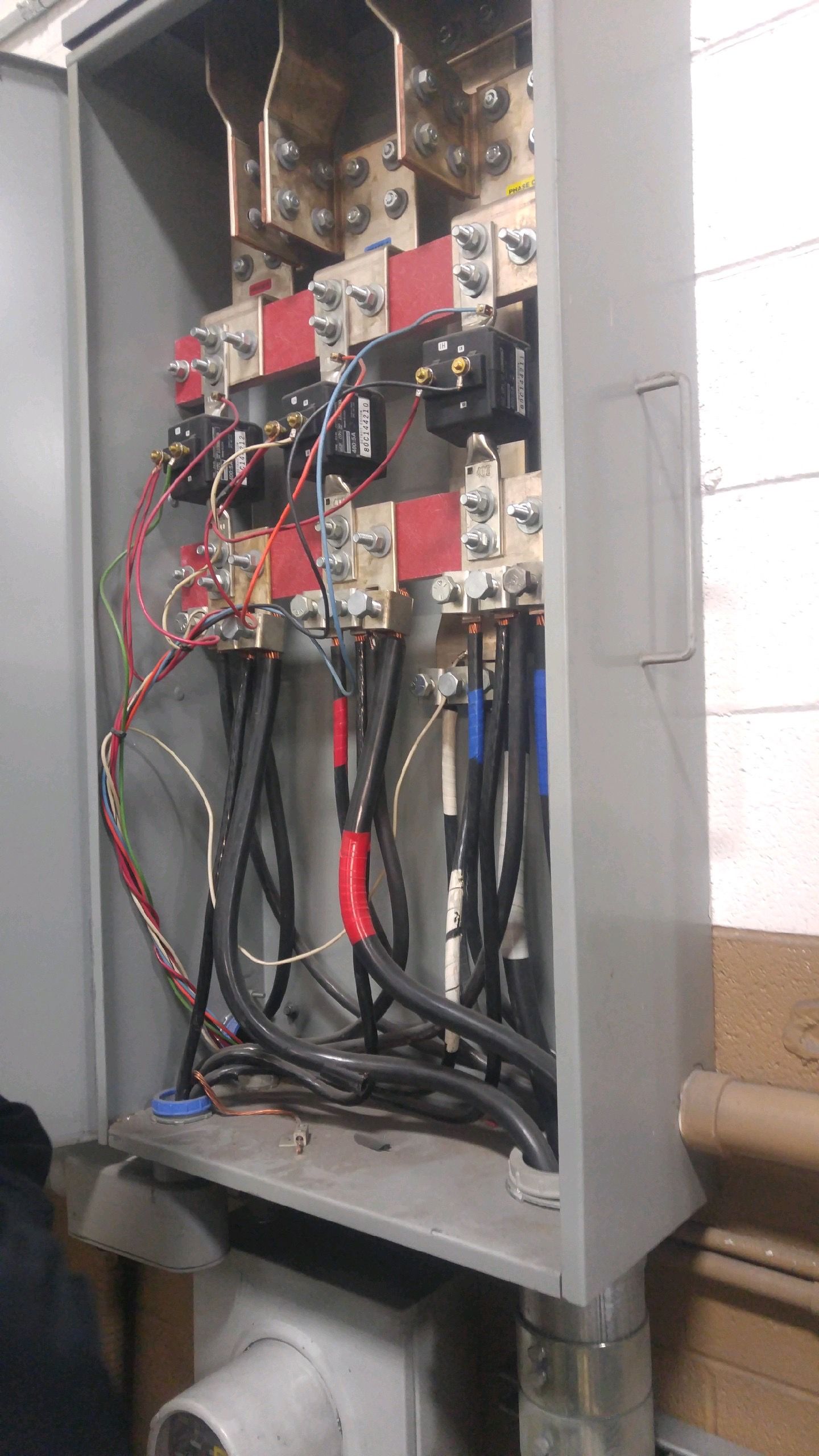 Open electrical panel with wiring, breakers, and red relays inside a gray cabinet.