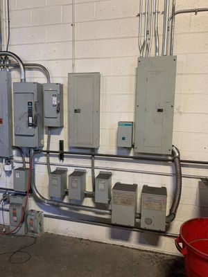 Electrical panels and conduit mounted on a cinder block wall in an industrial utility room.