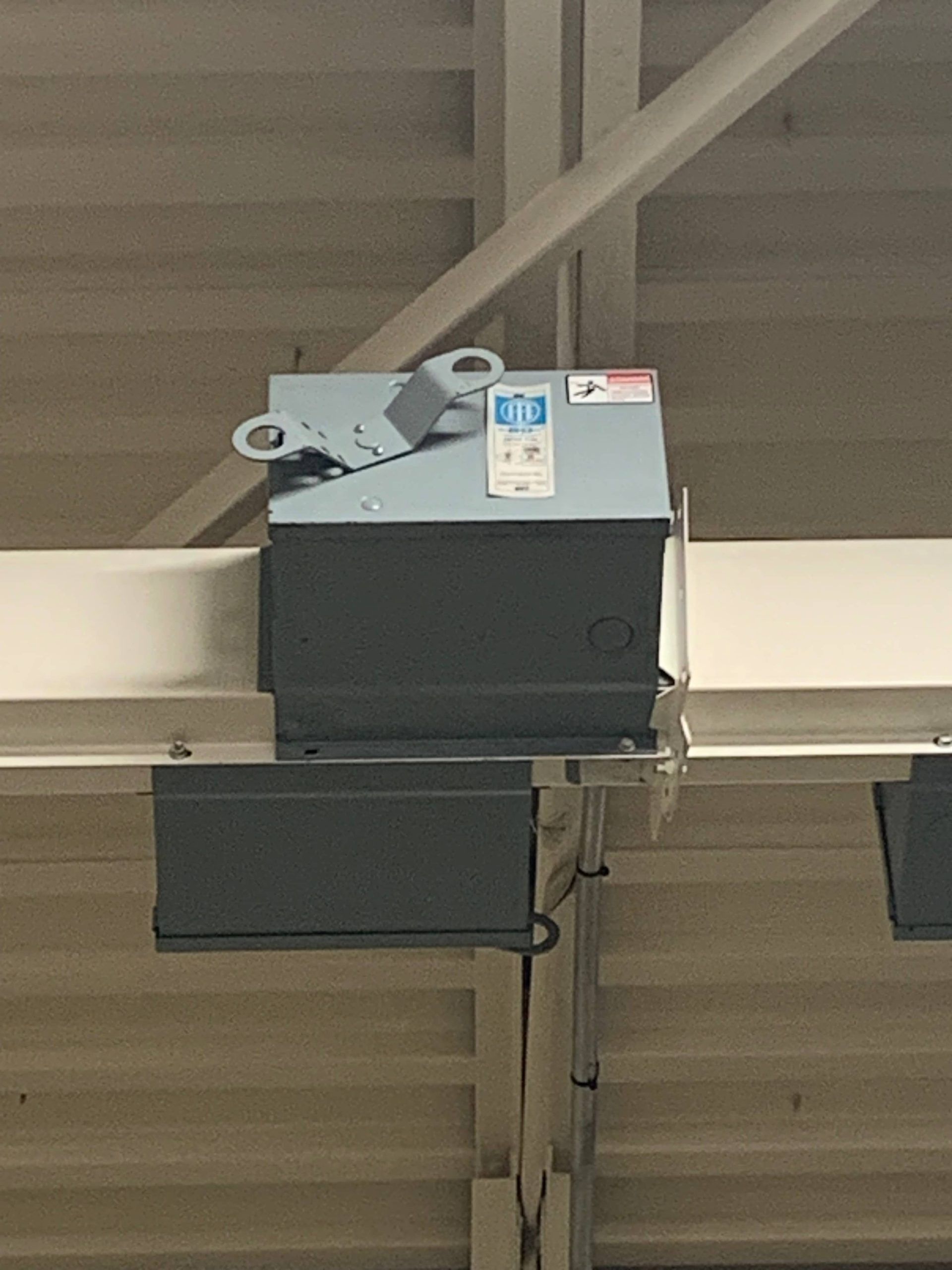 Gray industrial device mounted near the ceiling with brackets and a hanging cable.