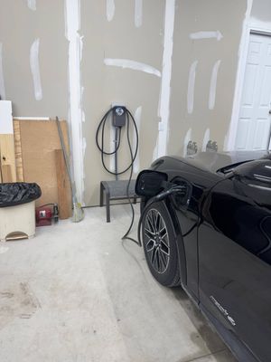 Black sports car parked in a garage beside unfinished drywall and a white door