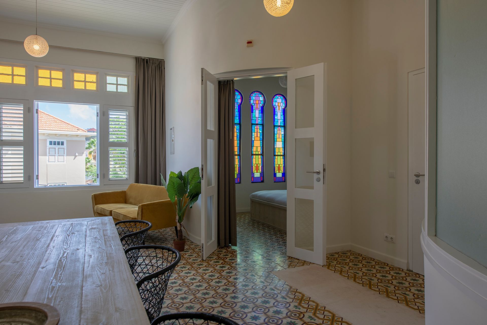 A bedroom with a bed , chair , table and stained glass windows. t Klooster Hotel Curacao