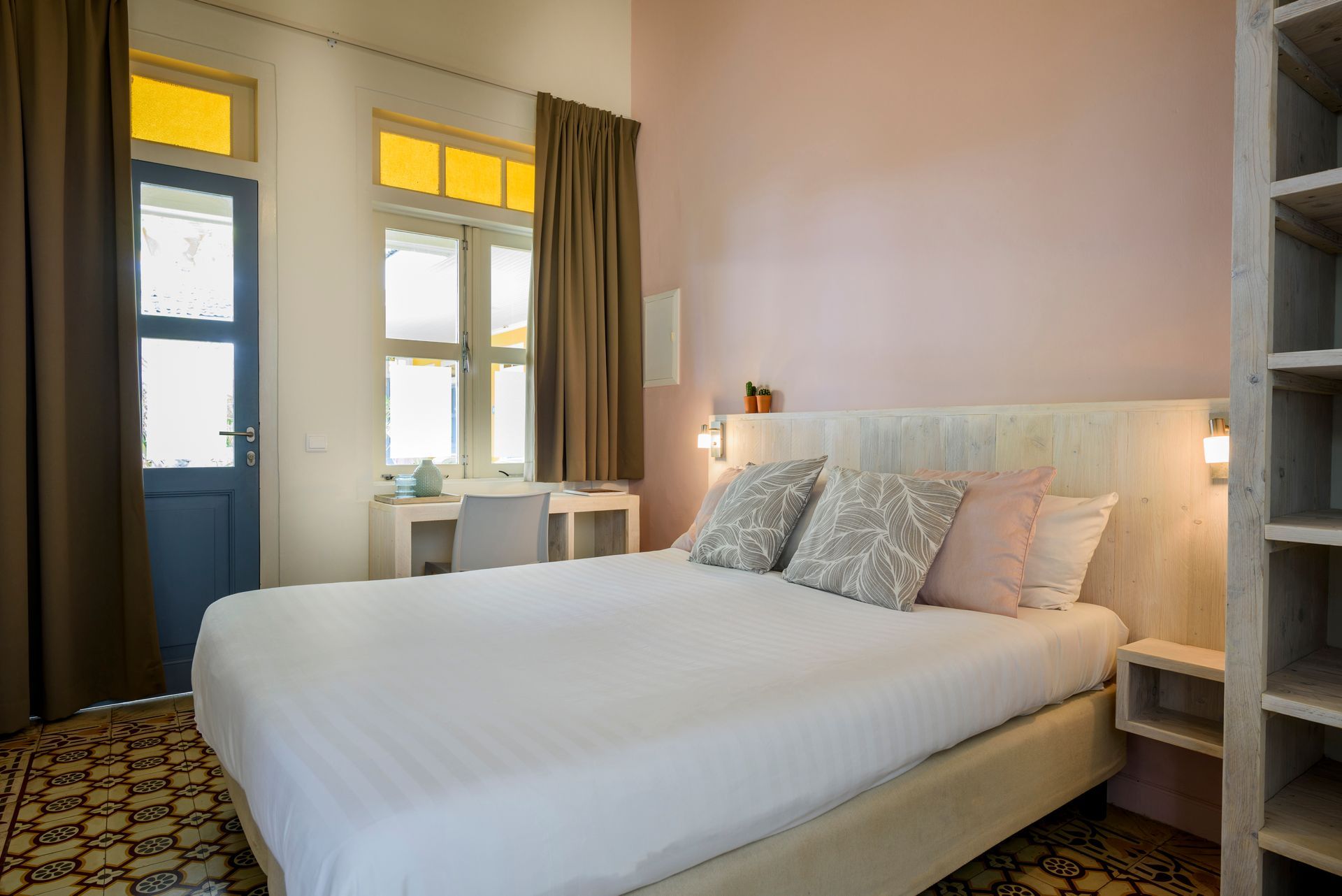 A bedroom with a king size bed , a desk , and a blue door. t Klooster Hotel Curacao