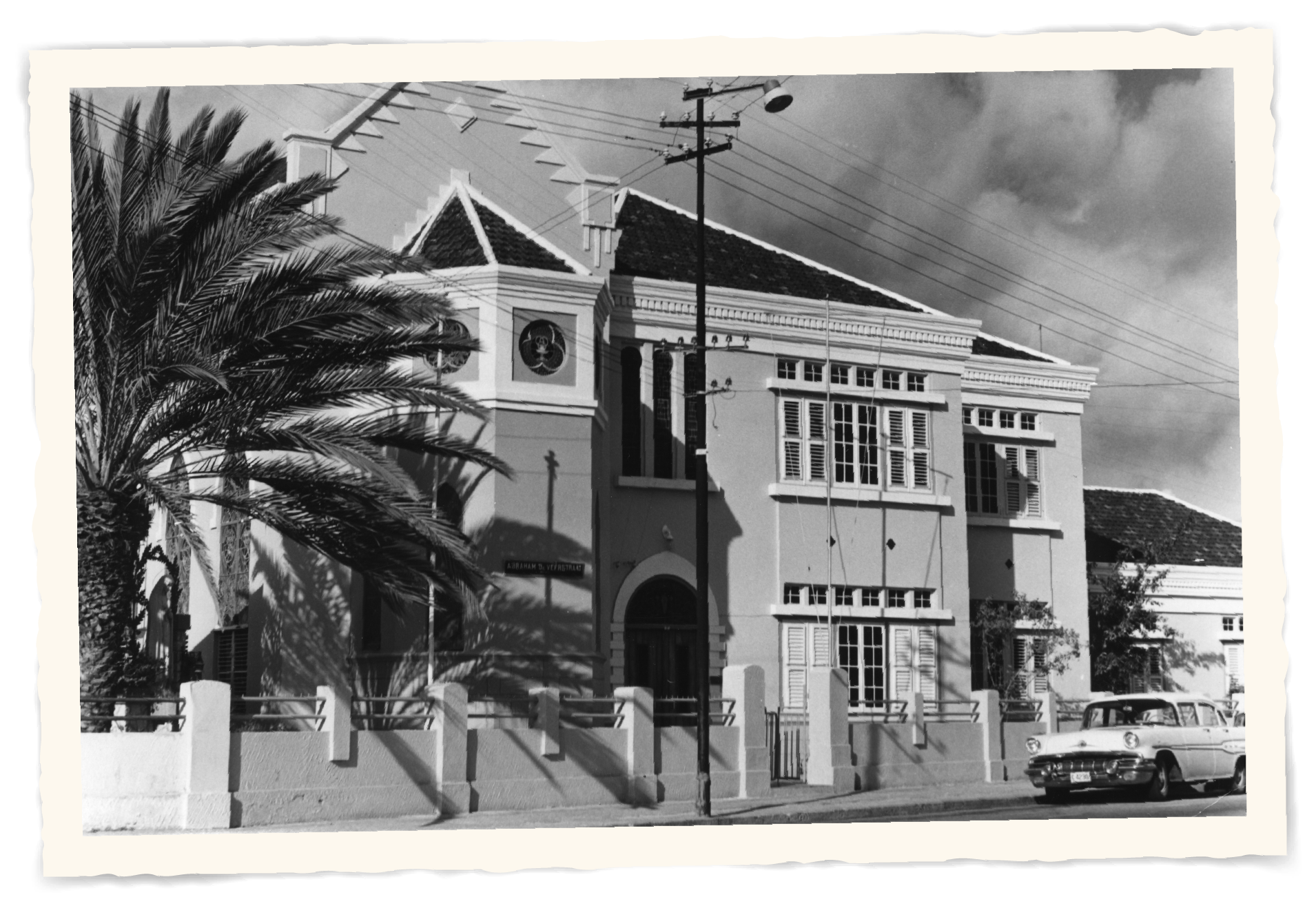 A black and white photo of a building with a palm tree in front of it t Klooster Hotel Curacao