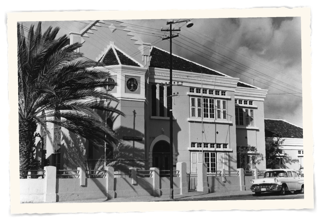 A black and white photo of a building with a palm tree in front of itt Klooster Hotel Curacao