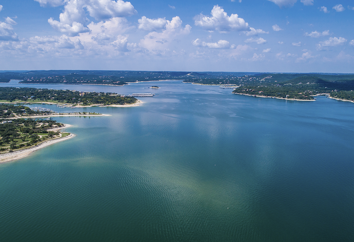 Aerial view of a wide blue lake with green shores under a partly cloudy sky.