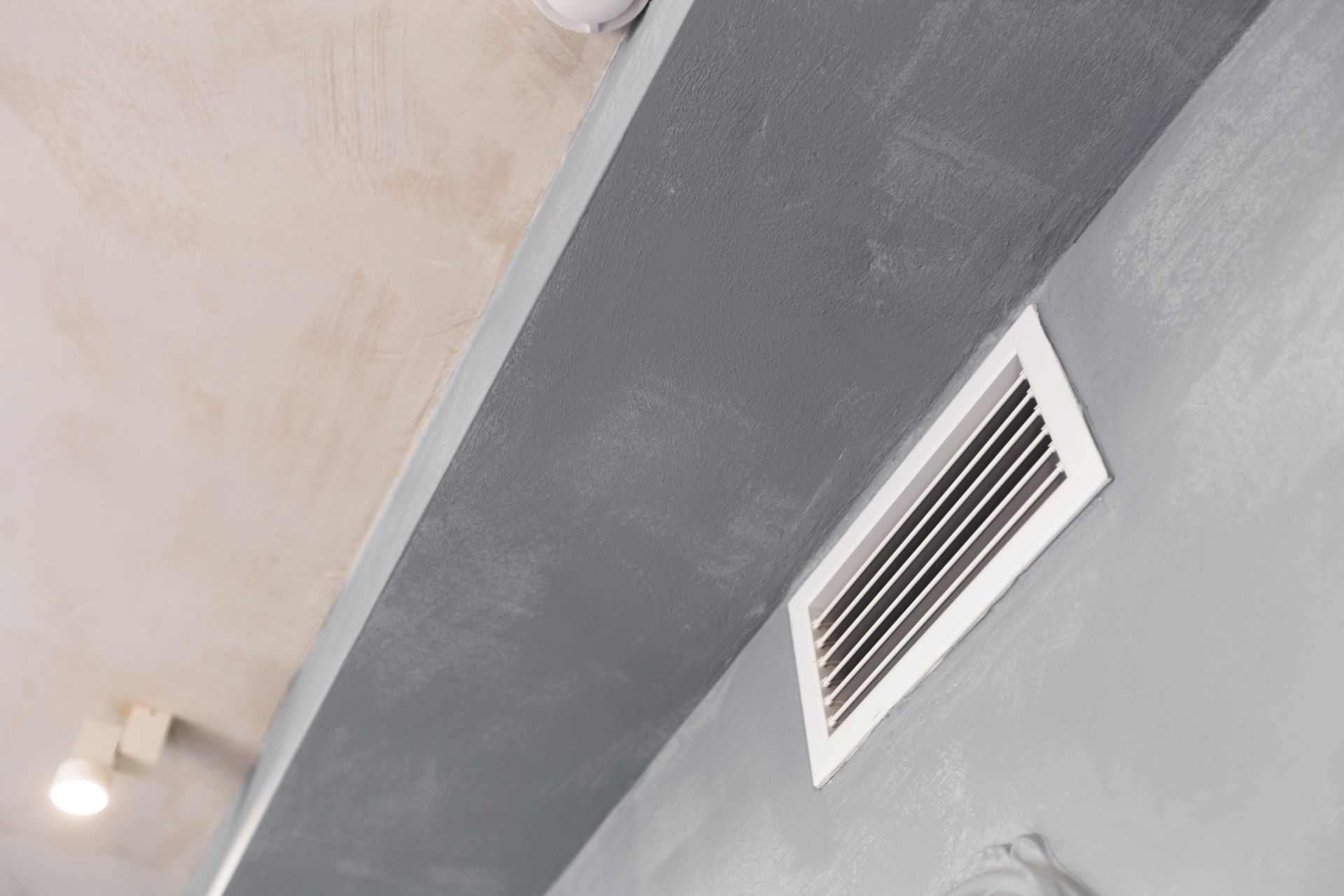 Gray wall and ceiling with a white vent and a light.