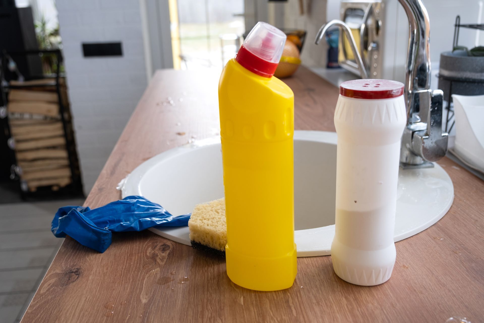 Cleaning supplies on a kitchen counter, including a yellow bottle and a white bottle by the sink.