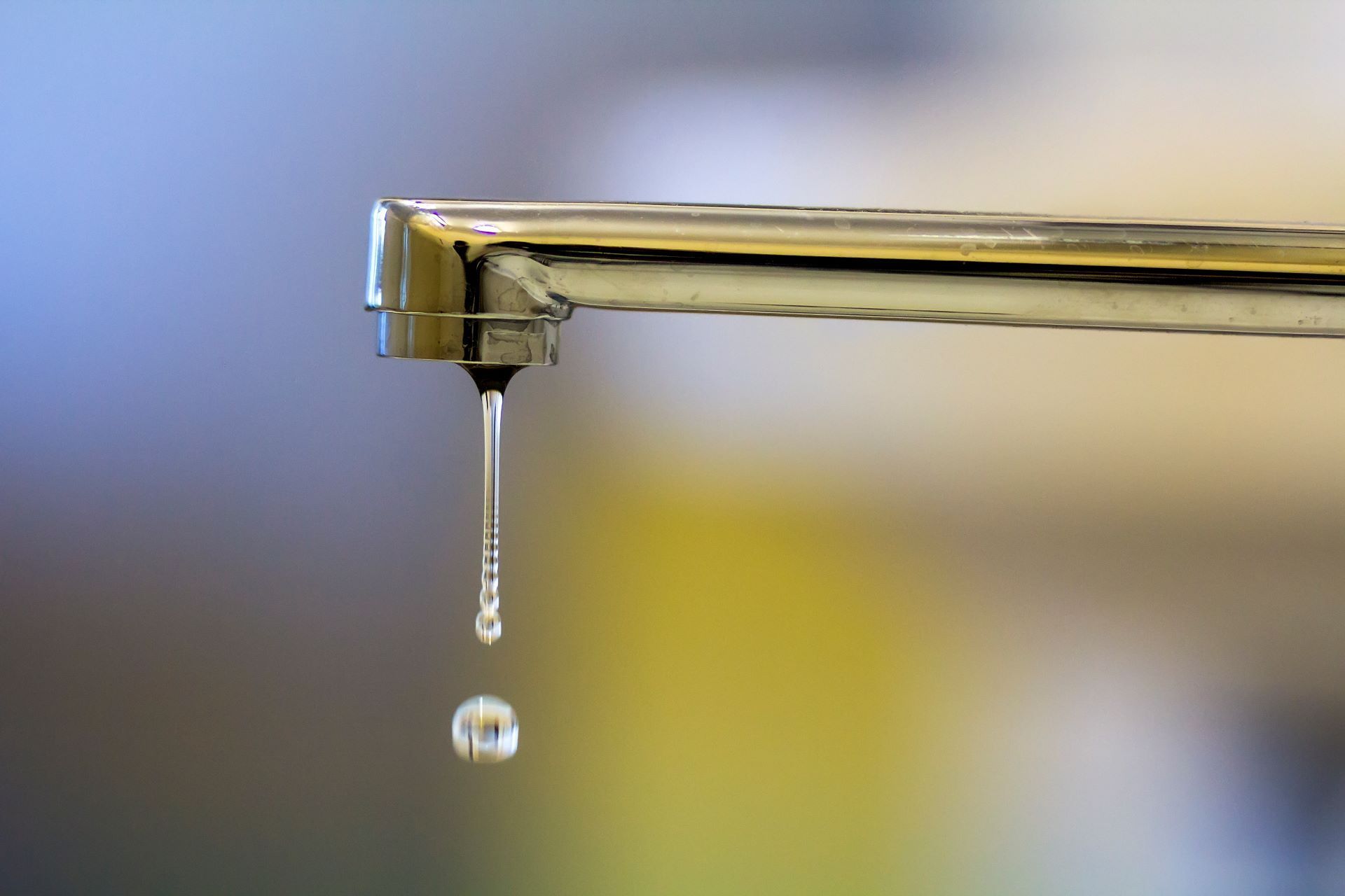 Close-up of a chrome faucet with a single water droplet falling.