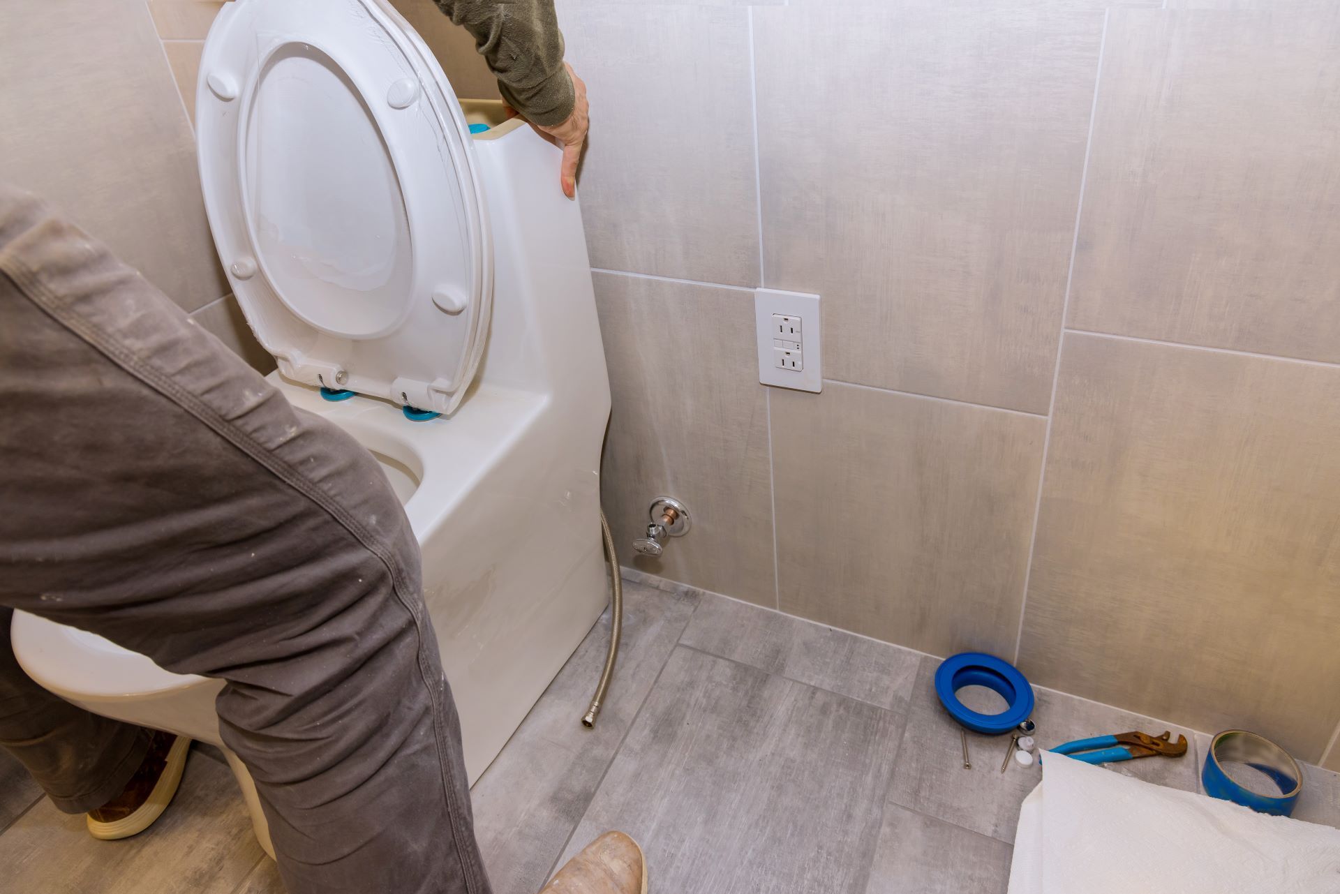 Person installing a toilet in a bathroom, near a wall with an electrical outlet.