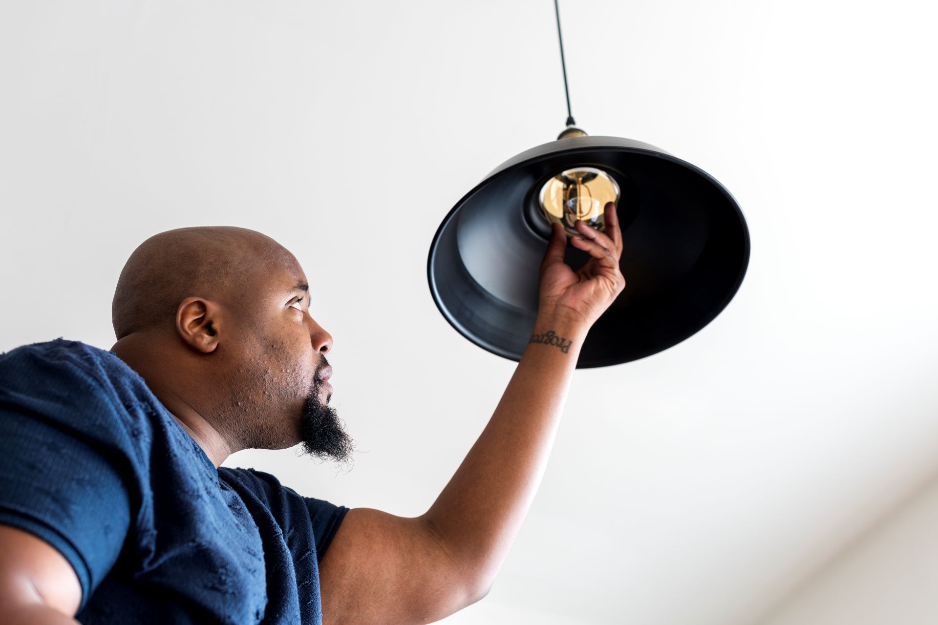 Man replacing a lightbulb in a black pendant lamp, looking up intently.